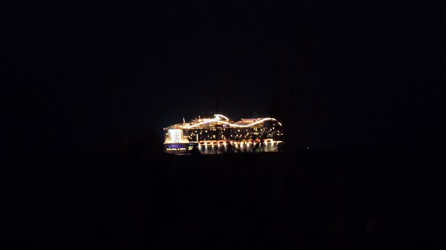 Nighttime view of the MSC World Europa cruise ship glowing with bright lights as it sails across the dark ocean. The futuristic design and reflections on the water create a striking scene.