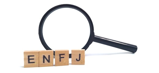 Wooden blocks with ENFJ letters, and a magnifying glass. ENFJ is one of the 16 personality types identified by the Myers-Briggs Type Indicator or MBTI. Concept of psychology.
