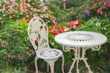 White chairs and table in patio around with colorful flowerbed. Flower garden small patio with...