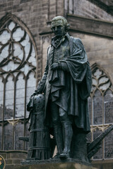 Statue of a prominent historical figure in Edinburgh overlooking a historic church