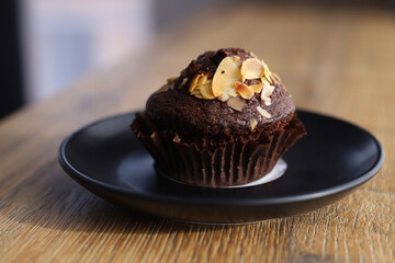 chocolate cupcake sprinkled with nut shavings on a black saucer that stands on a wooden table