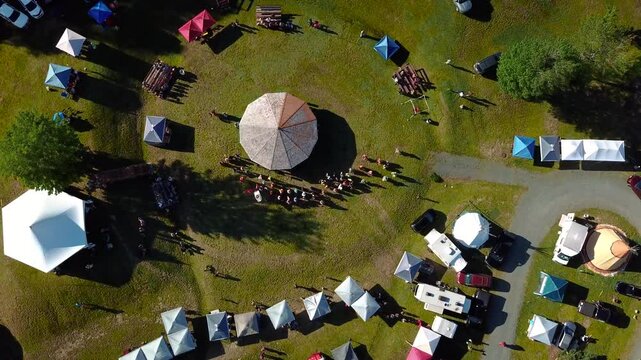 Bird"s-eye view of a Powwow event. Tents are set in a circular pattern. The drone shot rotates by following the pattern.