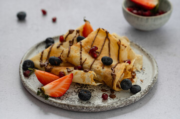 Crepes, blinis or thin pancakes with strawberries, chocolate and blueberries on a plate on stone table. Sweet Breakfast or Brunch. Maslenitsa, Mardi grass traditional meal.