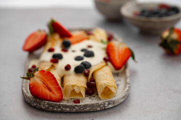 Crepes, blinis or thin pancakes with strawberries, whipped cream and blueberries on a plate on stone table. Sweet Breakfast or Brunch. Maslenitsa, Mardi grass traditional meal.