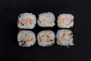 Top view of Six shrimp sushi maki rolls wrapped in nori, served on a black slate plate. A simple and elegant Japanese dish with fresh ingredients and delicate presentation.