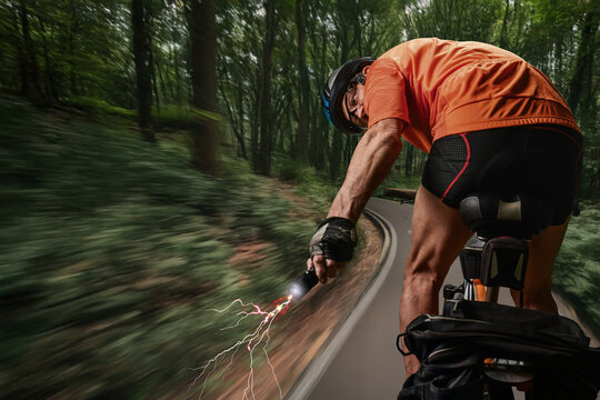 Sporty man riding bike in forest and holding in hand ultrasonic dog repeller. Man cycling through forest carries stun gun, prioritizing safety against unexpected dog encounters.