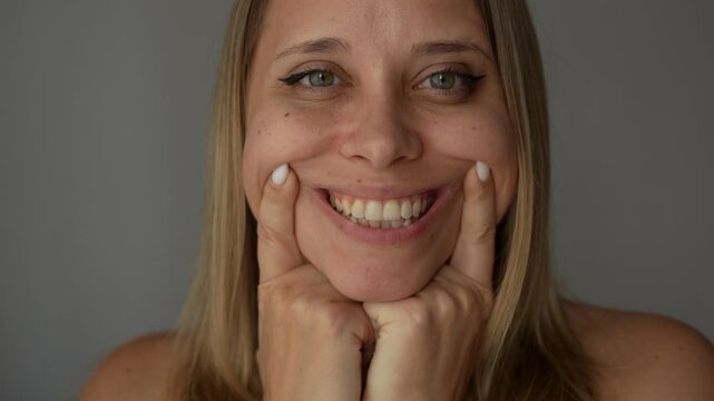 Young caucasian blonde woman showing the smile pulling it with her hands on a dark grey background. Teeth whitening. Oral hygiene, dental health care, perfect even teeth. Dentistry
