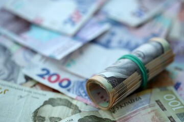 Roll of 500 Ukrainian Hryvnia money bills lies on big pile of ukrainian currency money close up