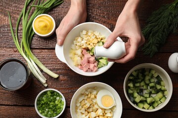 Making okroshka soup. Woman adding salt into bowl with different ingredients at wooden table, top...