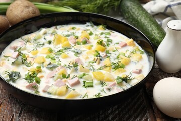 Delicious okroshka soup with kefir in bowl and ingredients on wooden table, closeup