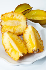 Two whole fresh ripe pineapples or sweet baby ananas and starfruits on white background close up