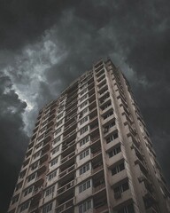Low-angle photograph of a tall building, with a gray concrete texture and a dark sky. 