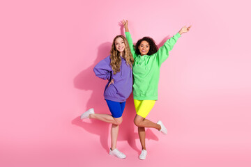 Two young friends in stylish hoodies posing cheerfully against a pink background, celebrating friendship and vibrant fashion