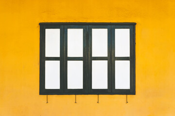 Obraz premium Classic old wooden windows with old metal shutter hook on edge. Old Closed vintage white and black wooden windows on the yellow cement wall. Simple, Beautiful and classic architecture of the house.