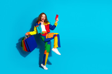 Happy woman holding shopping bags and taking selfie in colorful outfit against blue background