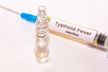 Picture on a white background with a syringe full of typhoid fever virus vaccines, and next to it...