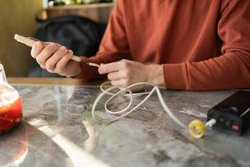 Close-up of male hands attaches smartphone to external power bank with charge cable at cafe or coworking space