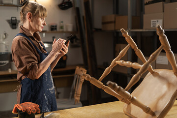 Busy female carpenter using mobile phone standing in her workshop. Start-up and sme