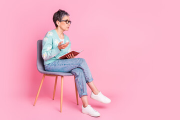 Elderly Woman Sitting on a Chair Holding a Notebook Against a Pink Background, Reflecting and Gesturing Thoughtfully