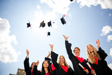 Cheerful graduates celebrating their success by tossing mortarboards into the sky on a sunny day