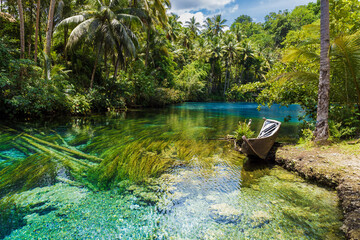 Clear lake with blue water and old boat in tropical forest in Indonesia.