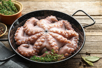 Fresh raw octopus and thyme in frying pan on wooden table, closeup