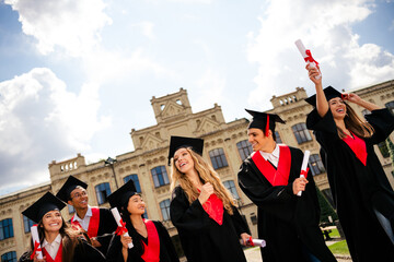 Joyful graduates celebrate achievement under bright summer sky at city campus, holding diplomas and...