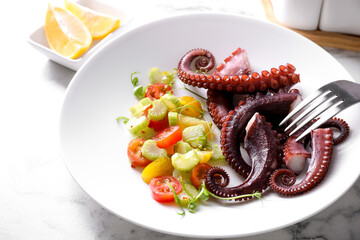 Plate with tasty boiled octopus tentacles, salad and fork on white marble table, closeup