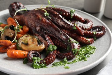 Roasted octopus with vegetables and mushrooms on table, closeup