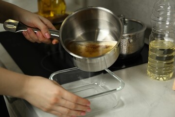 Woman pouring used cooking oil into glass container at white marble countertop, closeup