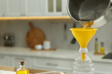 Pouring used cooking oil into bottle through funnel in kitchen, closeup. Space for text