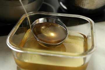 Used cooking oil in glass container and ladle on white countertop, closeup