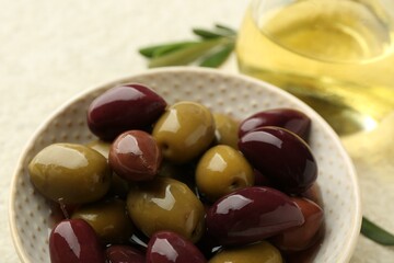 Tasty marinated olives in bowl and oil on beige table, closeup