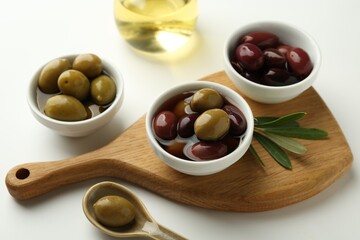 Tasty marinated olives, leaves and oil on white table, closeup