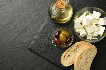 Delicious marinated olives, bread and feta cheese served on black table, top view. Space for text
