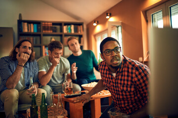 Young group of male friends watching a sports game in the living room on the tv and cheering for their team