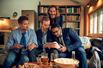 Young group of people using a smart phone while watching a sports game in the living room