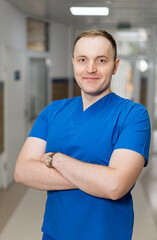 Confident medical pro in scrubs. A skilled healthcare worker stands in a hospital hallway, smiling and ready to assist patients in need of care.