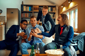 Young group of people using a smart phone while watching a sports game in the living room
