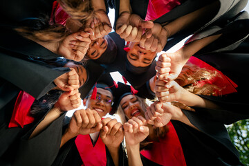 Low ange view photo of groupmates students hands make circle mortarboard gown graduate college outdoors