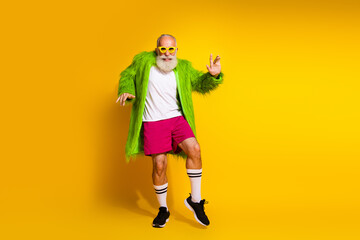 Elderly man embracing unique style wearing vibrant clothes against yellow background expressing...