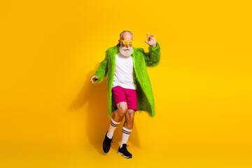 Energetic elderly man in vibrant green fur coat showcasing fun and eccentric style on vivid yellow background