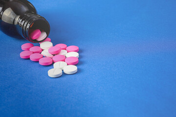 Pink and white medicine pills spilling out of a dark bottle on a blue background, representing healthcare and pharmaceutical concepts