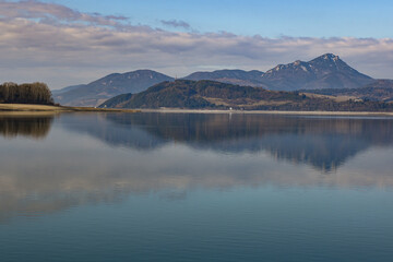 Calm water reflecting surrounding hills and cloudy sky at liptovská mara lake in slovakia