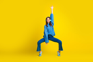 Young Woman in Blue Sweater Posing Playfully on Vibrant Yellow Background