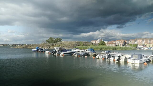 Farbenfrohe schwedische H&auml;user und malerische Boote an der Ostseek&uuml;ste bilden eine idyllische Szene unter einem dramatisch bew&ouml;lkten Himmel, der die Landschaft verzaubert.