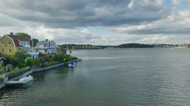 Farbenfrohe schwedische H&auml;user und malerische Boote an der Ostseek&uuml;ste bilden eine idyllische Szene unter einem dramatisch bew&ouml;lkten Himmel, der die Landschaft verzaubert.