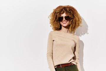 woman with curly hair wearing sunglasses, smiling confidently, casual fashion, light background,...