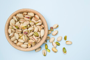 Pistachio nuts into wooden bowl on light blue background. Top view.