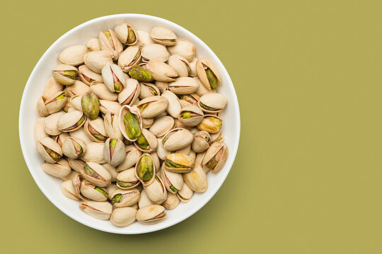 Pistachio nuts into bowl on green background. Top view.